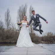Bruidegom springt gat in de lucht op steiger naast lachende bruid , spontane trouwfoto.