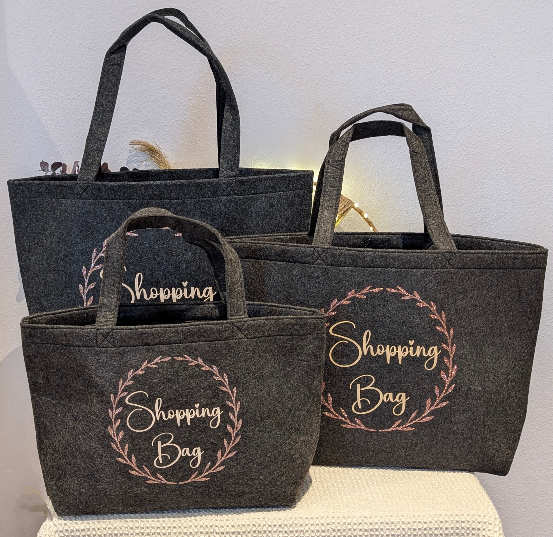 Shopperbeutel aus Filz in 3 verschiedenen Größen. Farbe dunkelgrau mit Aufschrift Shjopping Bag in beige und einem, Kranz in rosegold Glitzer.
