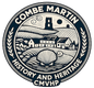 This circular logo represents the cultural and historical identity of Combe Martin, a village in North Devon, England. The design features a stylized rural landscape with rolling hills, a cluster of village buildings, and a prominent church tower.