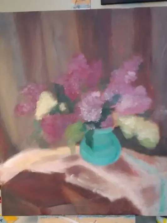 The easel with a canvas with the next stage of the painting process of a still life of lilac.