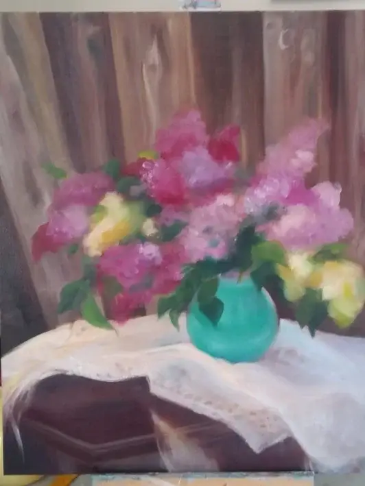 The easel with a canvas with the next stage of the painting process of a still life of pink lilacs.