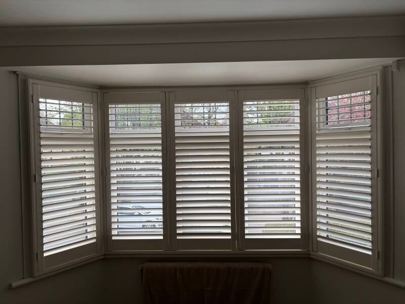Custom white plantation shutters fitted to a large bay window in a Canterbury home.