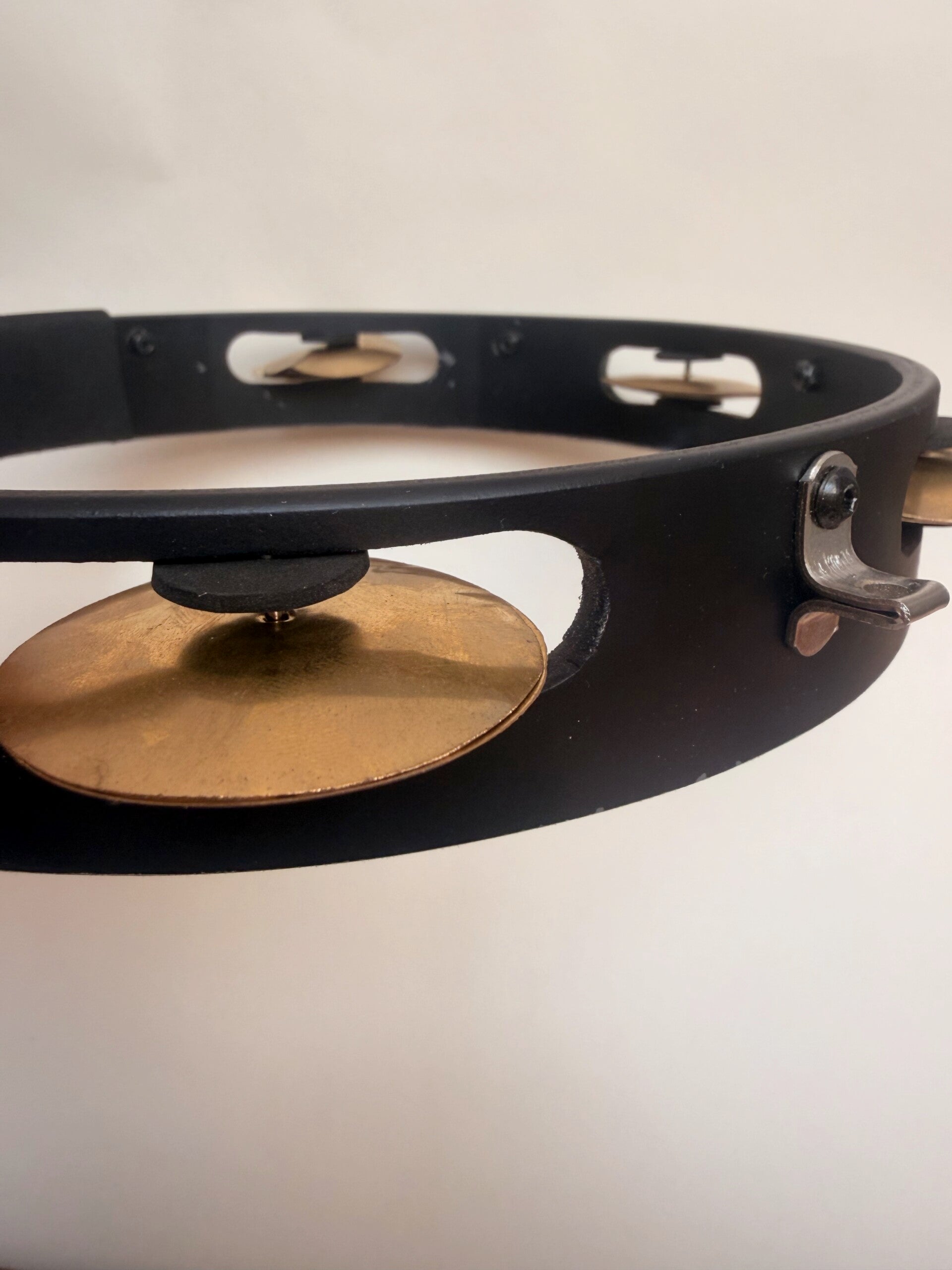 Gros plan du cadre noir en PVC et d’une cymbalette dorée d’un pandeiro artisanal pour la capoeira.