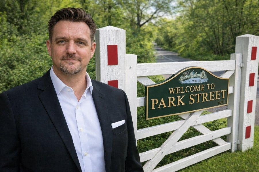 Neil Hughes standing beside the Welcome to Park Street sign on a tree‑lined road