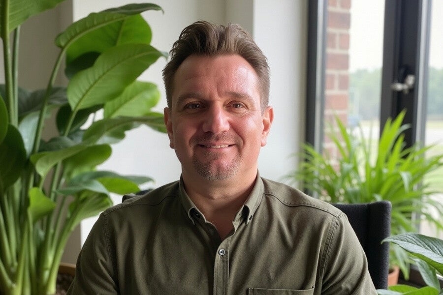 Portrait of Neil Hughes sitting indoors with natural light and plants in the background.