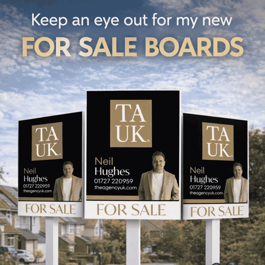 Black and gold TAUK For Sale boards featuring Neil Hughes displayed outdoors against houses.