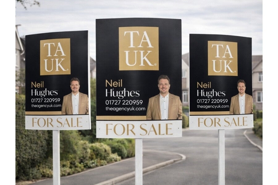 Black and gold TAUK For Sale boards featuring Neil Hughes displayed outdoors against houses.