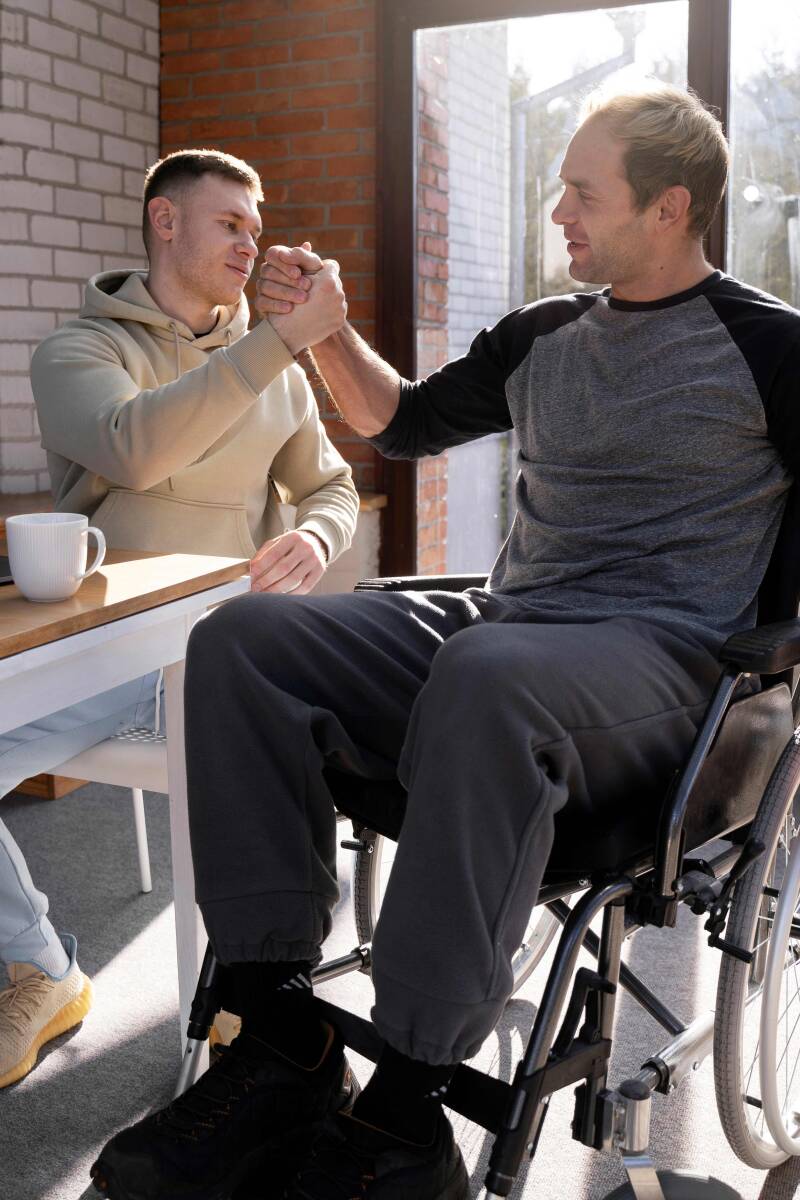 Mann, der wegen Multiple Sklerose im Rollstuhl sitzt, begrüßt seinen  Freund.