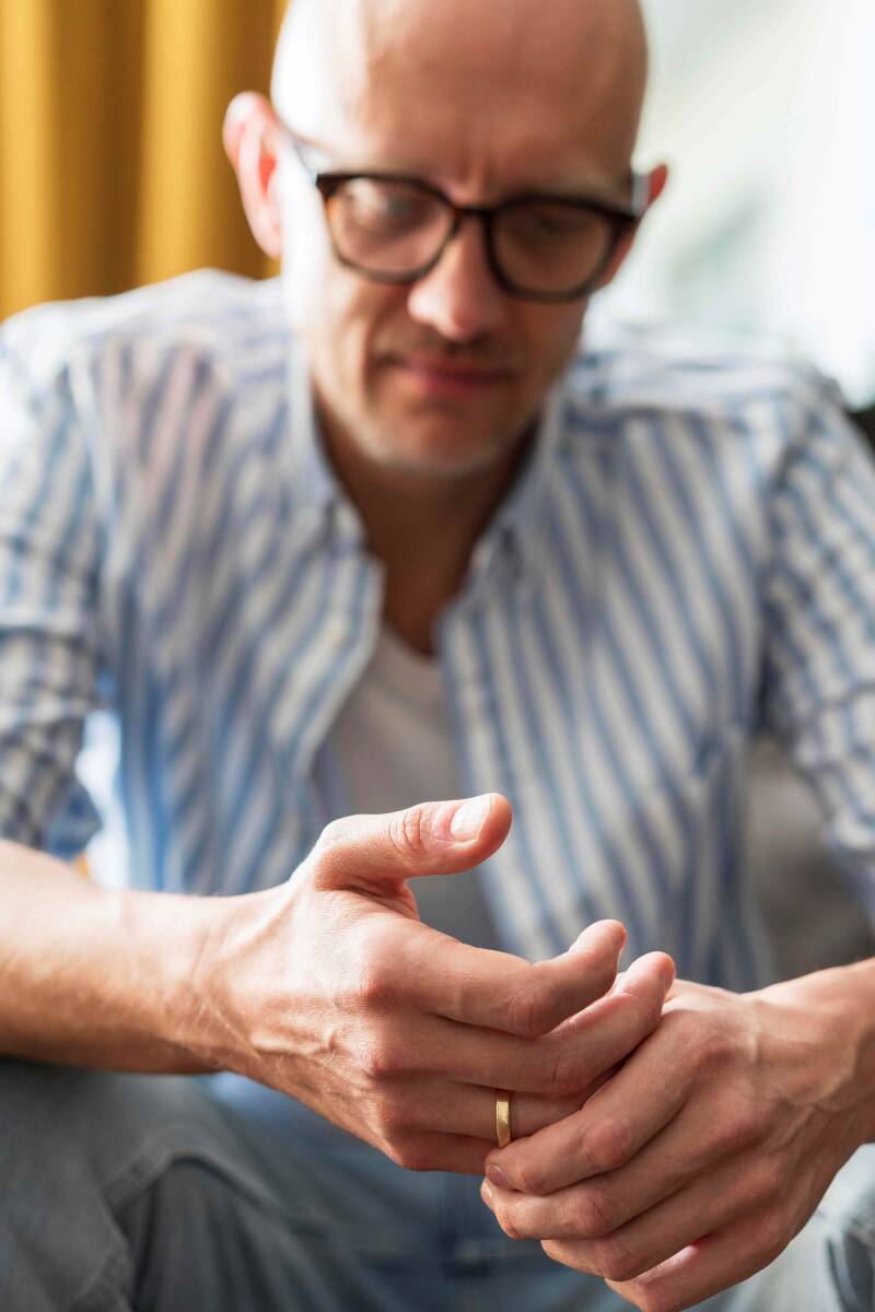 Ein Mann sitzt auf dem Sofa und reibt sich die Finger, denn er hat Nervenschmerzen in den Händen.