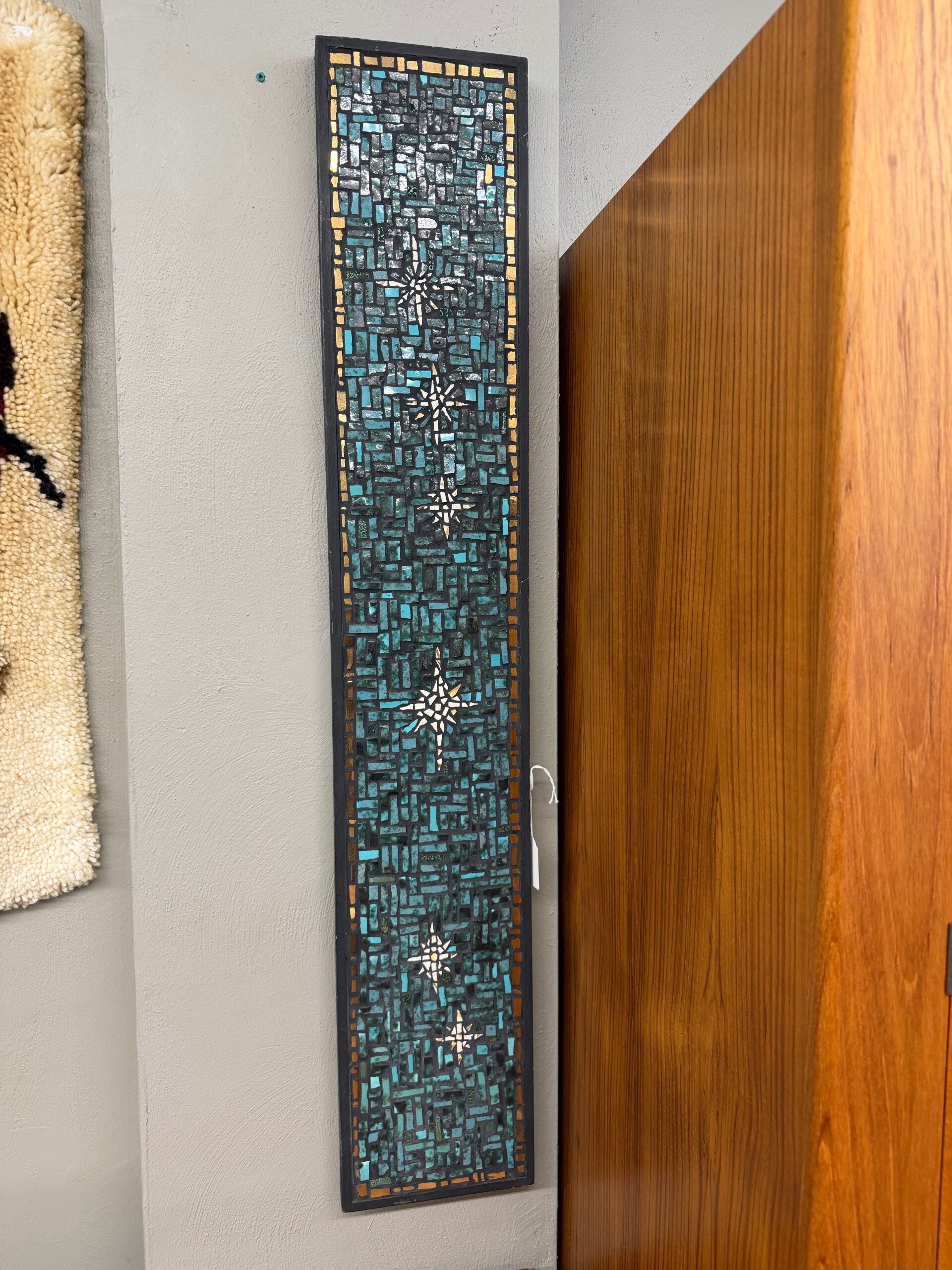 tall narrow mosaic wall art piece featuring a blue and teal tiled background with white star-like accents.