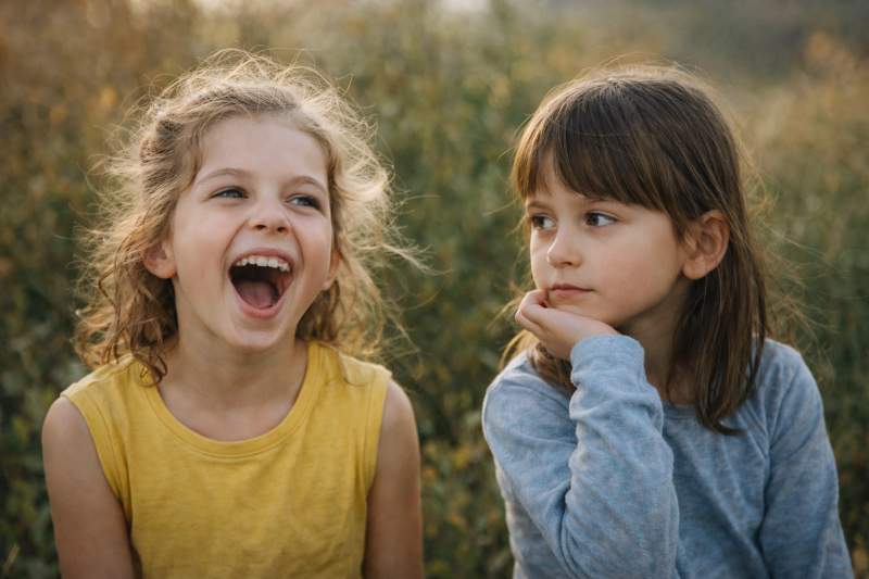 Zwei Kinder mit unterschiedlichen Persönlichkeiten: ein lebhaft lachendes Kind neben einem ruhig nachdenklichen Kind – Symbol für die Einzigartigkeit jedes Kindes.