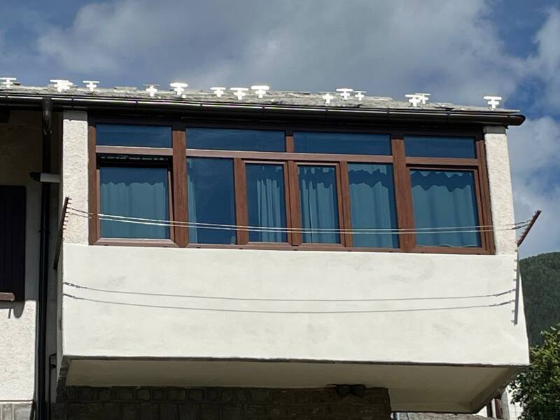 Serramento in PVC effetto legno installato su balcone in Valle d’Aosta, con ampie vetrate e profilo marrone realizzato da Briller Serramenti.