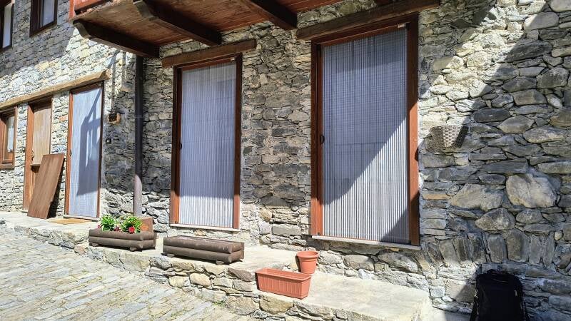 Installazione di zanzariere plissettate su misura su porte finestre in una casa rustica in pietra in Valle d’Aosta. Lavoro realizzato da Briller Serramenti.