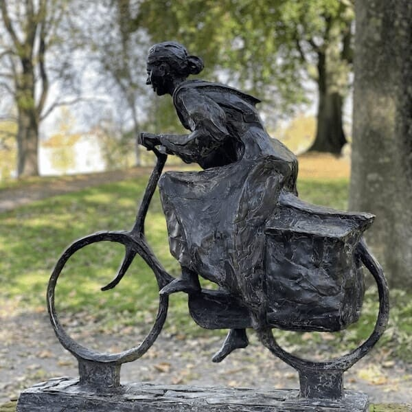 Beeldje van fietsende vrouw, voorovergebogen met zware fietstassen. Locatie Prinsentuin Leeuwarden.  Ontworpen door Andries Twijnstra