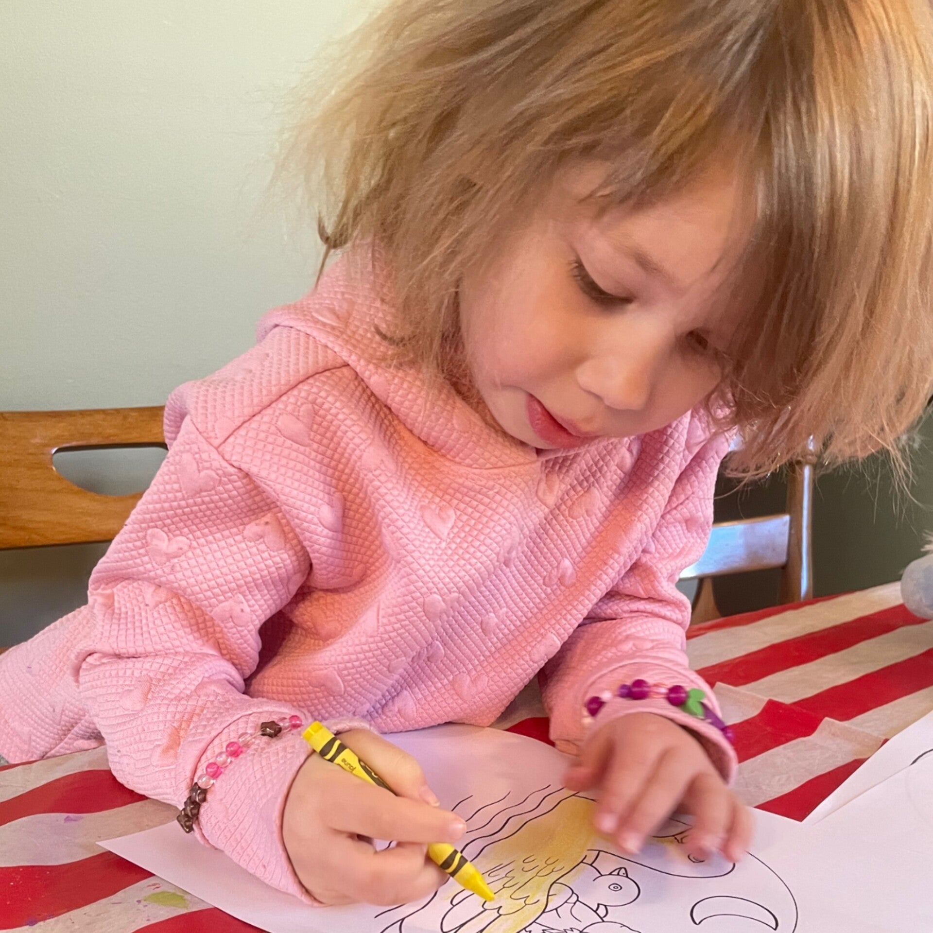Photograph of a little girl coloring a picture, holding a yellow crayon. 