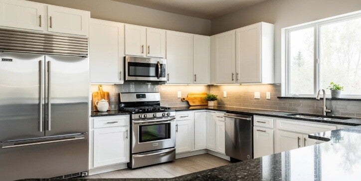 The image depicts a modern kitchen featuring newly installed stainless steel appliances, including an electric oven and a dishwasher, complemented by elegant granite countertops. This stylish space showcases the seamless integration of high-quality kitche