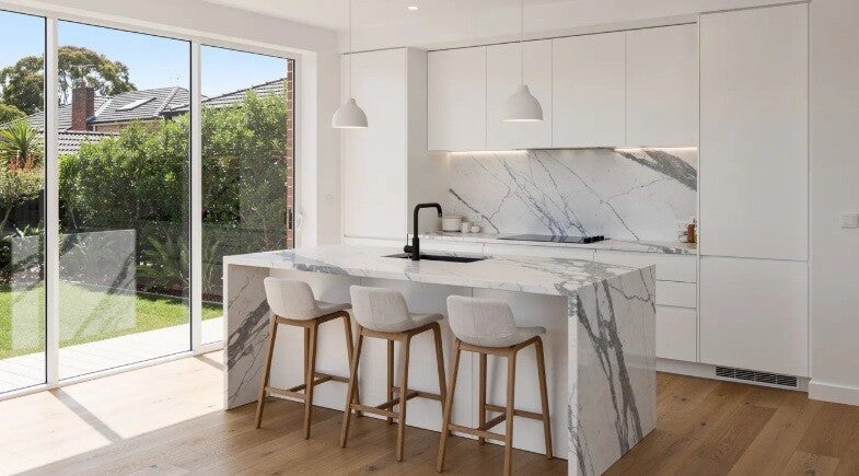 The image features a modern kitchen island with sleek waterfall stone edges, serving as a focal point in a bright Sydney home. This well-designed kitchen island includes integrated appliances and provides additional storage, perfect for casual dining and 