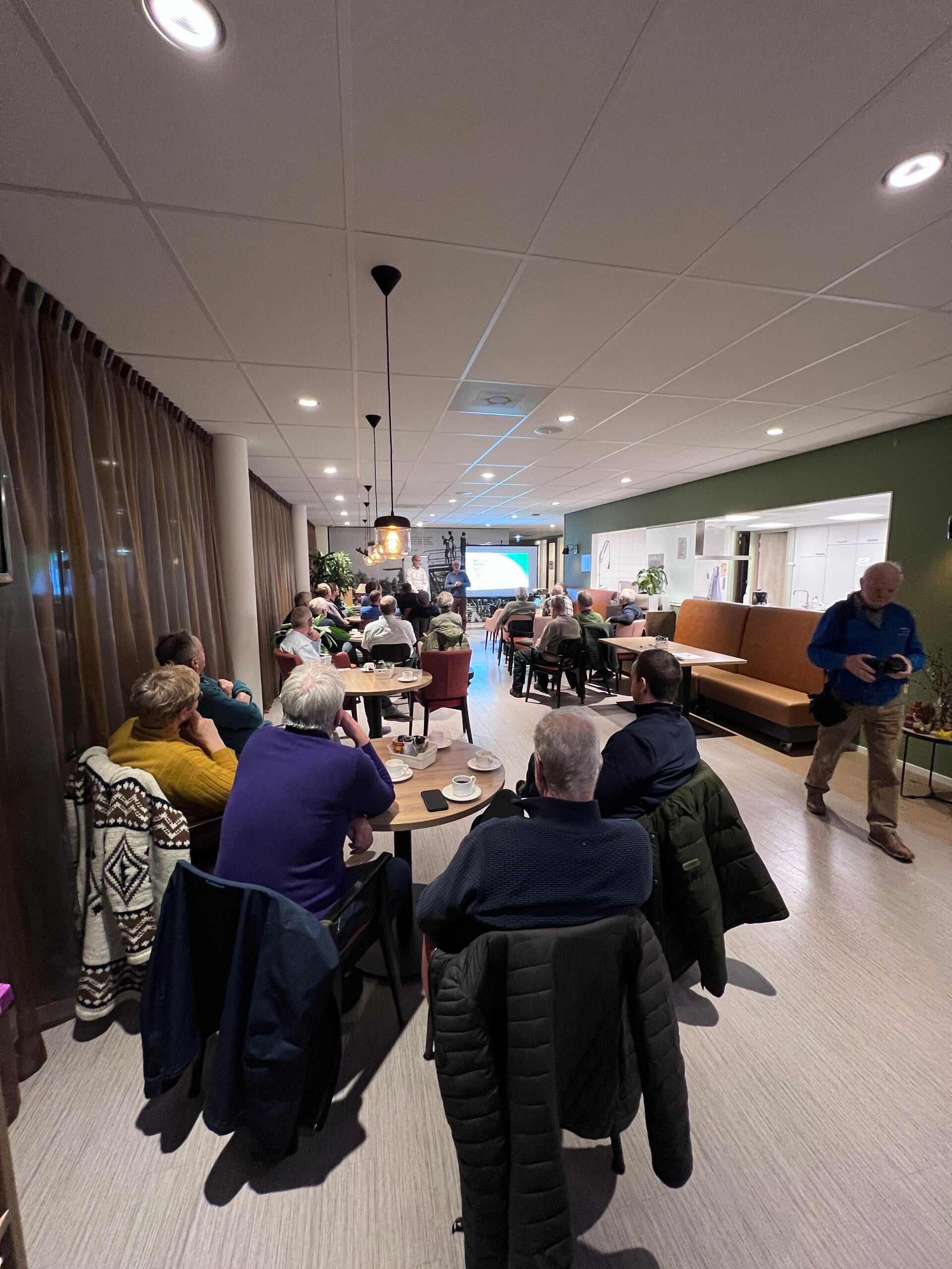 Toehoorders zitten te luisteren en te kijken naar een presentatie