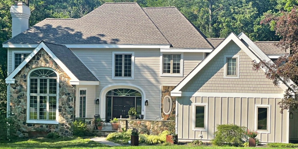 A modern two-story home featuring a stone facade, large windows, and a lush green lawn surrounded by trees.