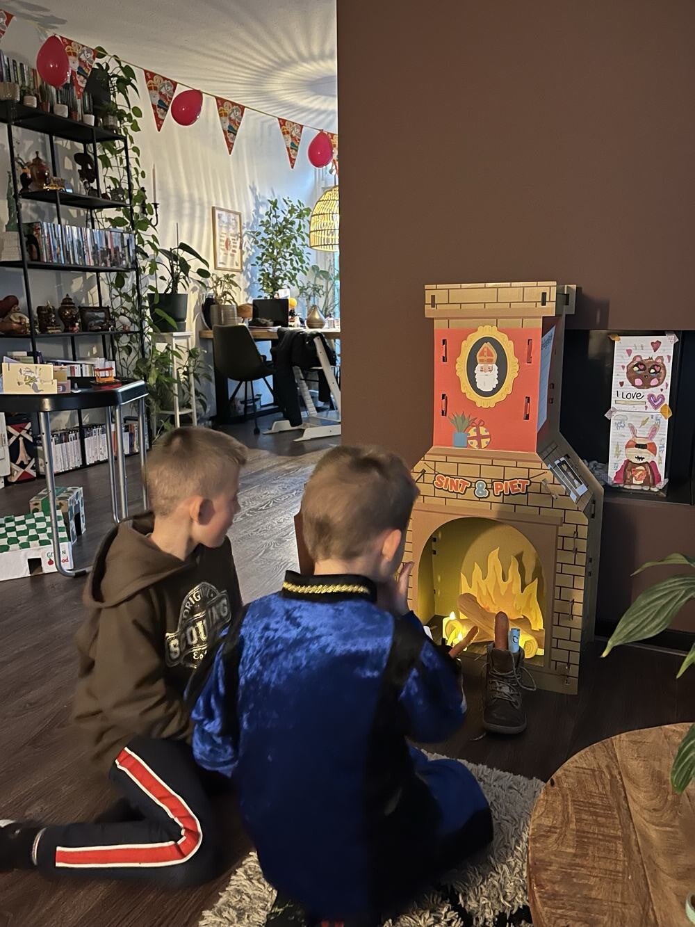 Twee kinderen zetten hun schoen bij een kartonnen Sinterklaas schoorsteen