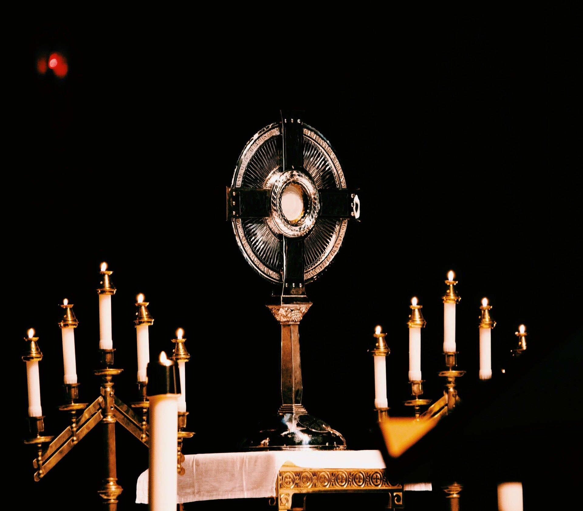 A monstrance with the Eucharist on an altar during Eucharistic adoration, surrounded by candles.