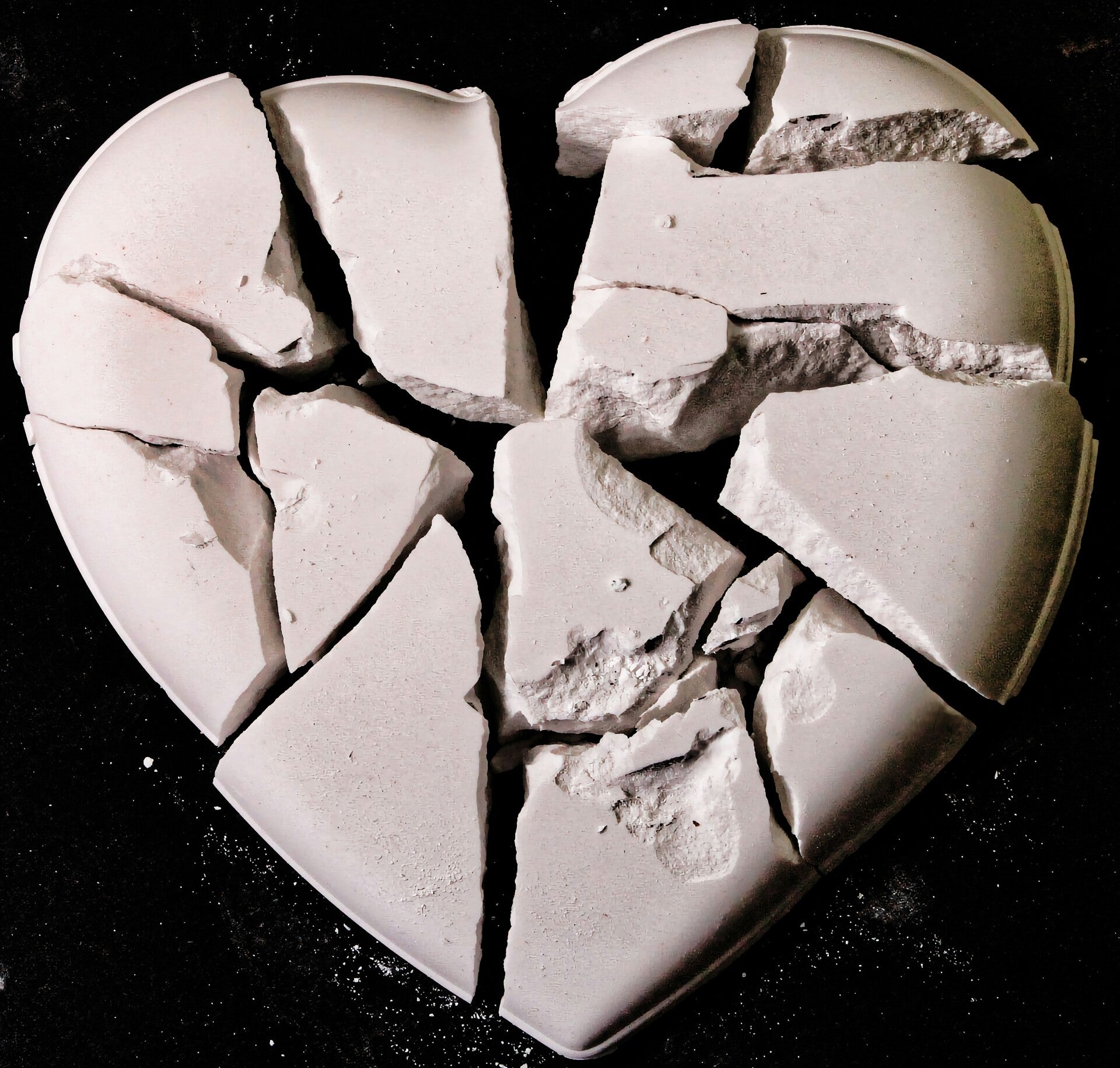 Whitish ceramic heart shattered against a black background.