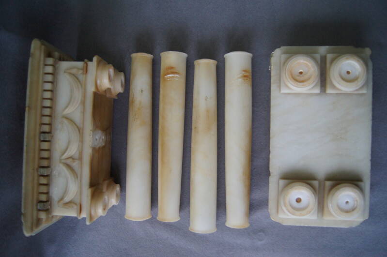 De albasten kolompendule in onderdelen.