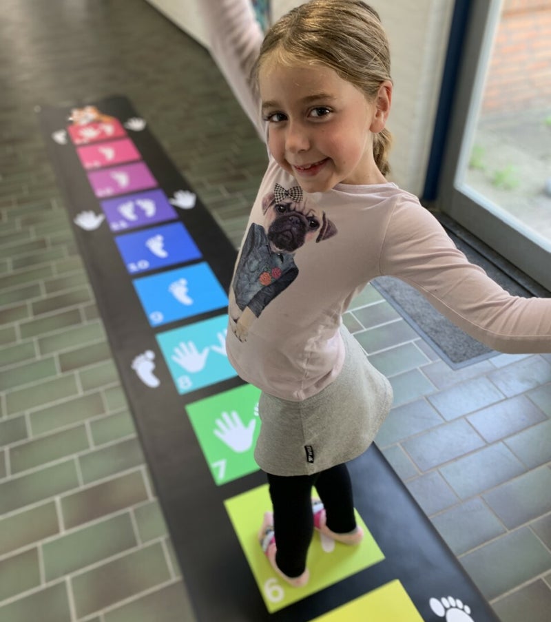 Op de beweegmat staan 14 gekleuerde vakjes met hand- en voetafdrukken er op.