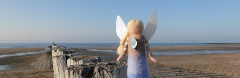 Wollen elfje op strand. Haar jurk heeft de kleuren van strand en zee - Wol & Lavendel - Naaldvilt