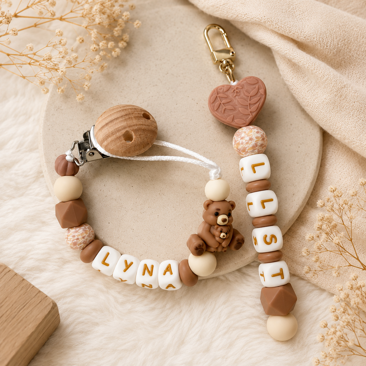 Handgemaakt geboortecadeau met gepersonaliseerd speenkoord en sleutelhanger met naam in zachte beige- en bruintinten, stijlvol gefotografeerd in een warme neutrale setting voor baby’s en kraamcadeaus.