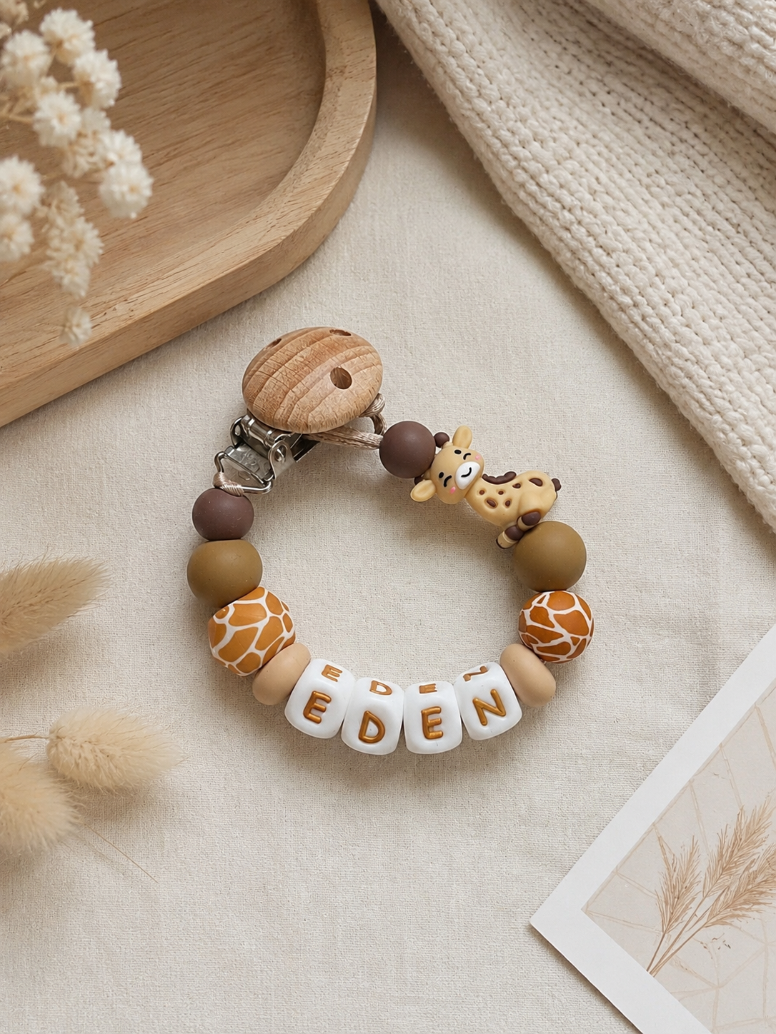 Handgemaakt gepersonaliseerd speenkoord met naam in roze tinten voor baby’s op zachte beige achtergrond