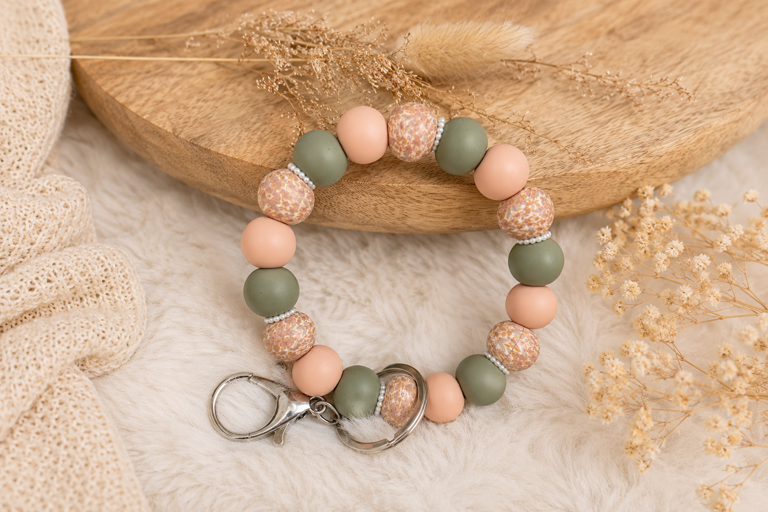 Handgemaakte sleutelwristlet met zachte groene en beige kralen op warme beige achtergrond