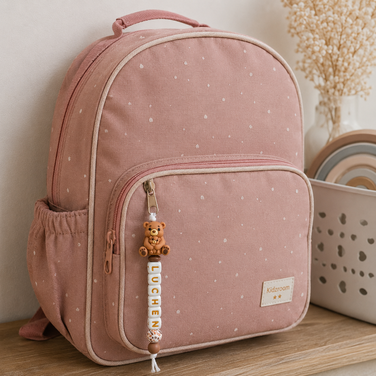 Handgemaakte gepersonaliseerde tassenhanger met naam voor kinderen aan roze rugzak op warme beige achtergrond