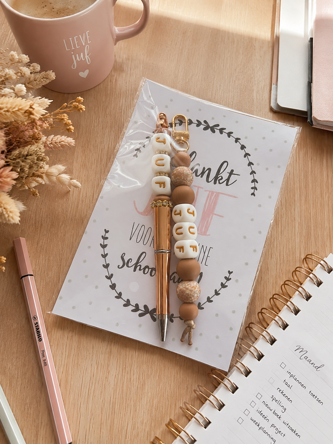 Handgemaakte kralenpennen voor juf of meester met kleurrijke “Best Teacher Ever” bedels, stijlvol cadeau voor leerkrachten, einde schooljaar of bedanking, gefotografeerd in een warme beige setting.