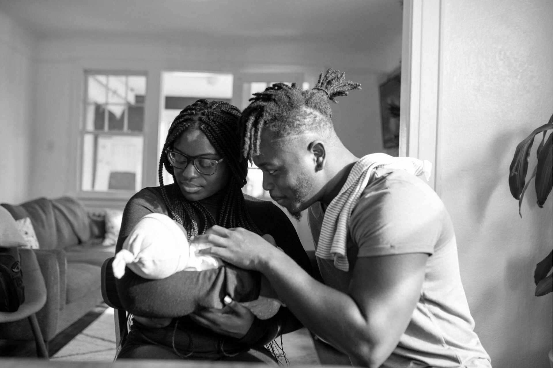 A woman holding a baby and a man next to her looking lovingly at the baby.