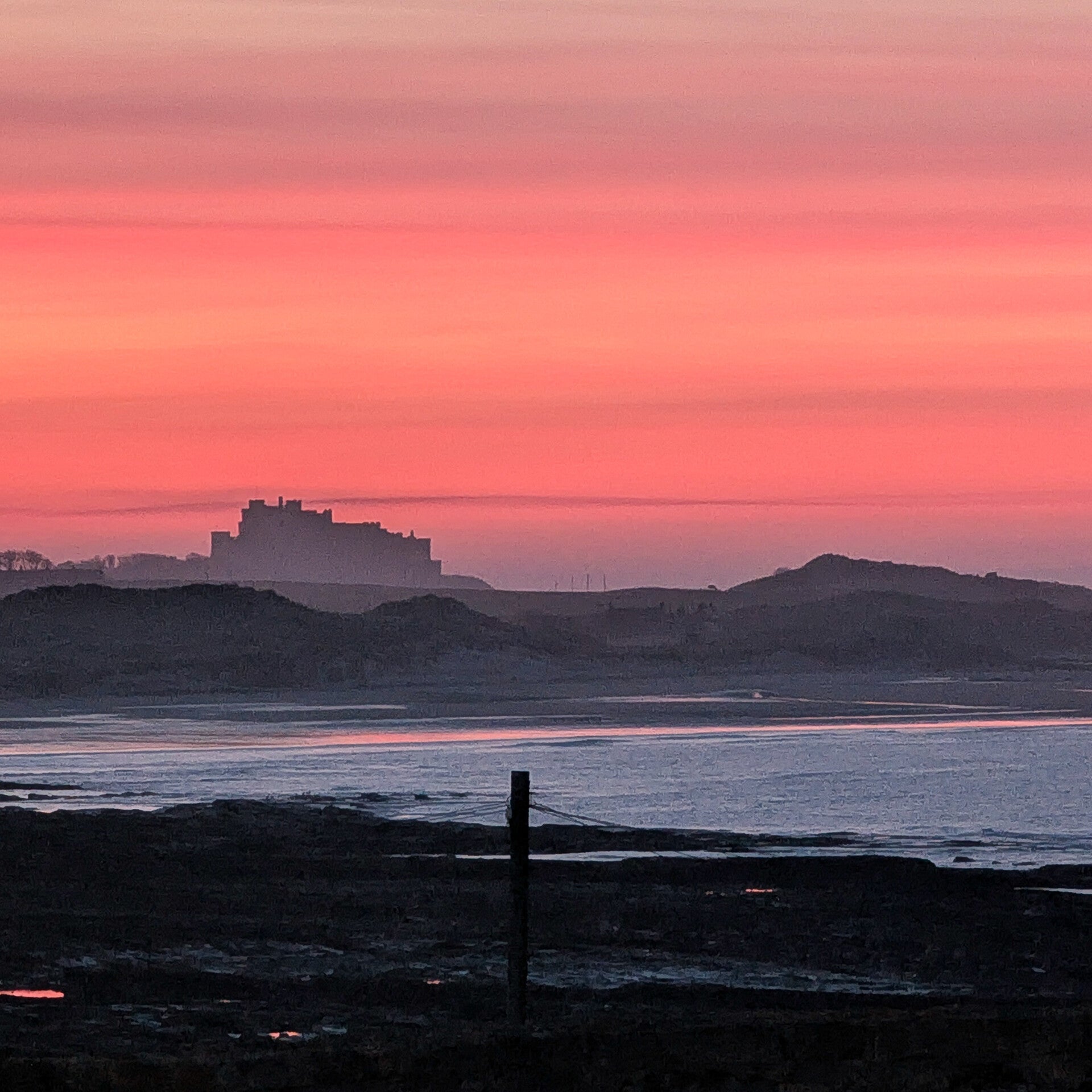 Bamburgh Castle silhouetted against a red sunset seen from Seahouses