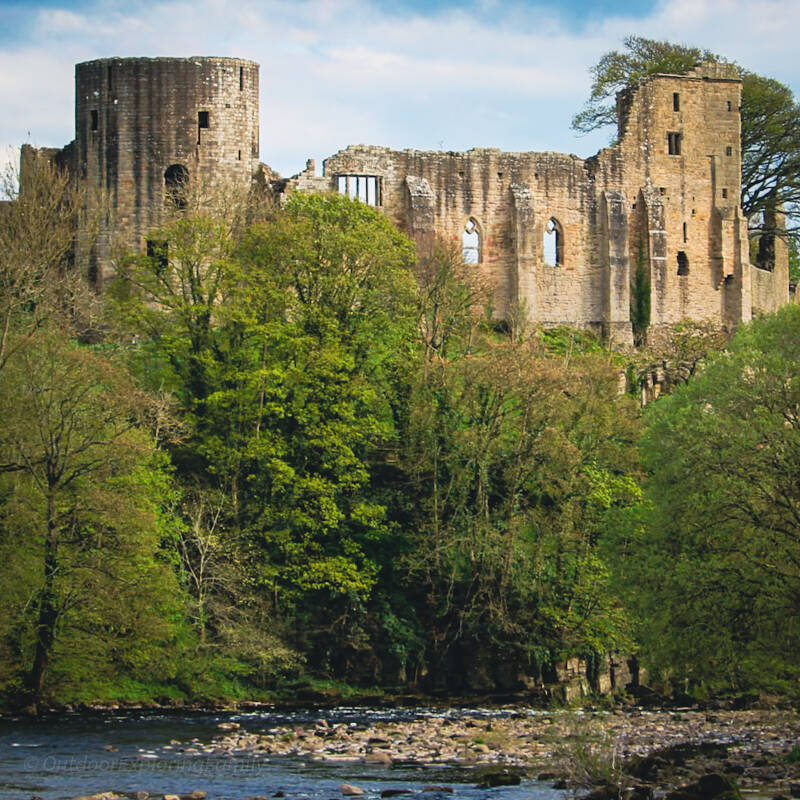 Barnard Castle ruins viewed from the River Tees with trees and flowing water below