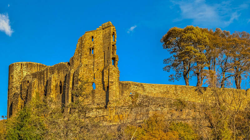 Barnard Castle ruins with the Round Tower, medieval stone walls and autumn trees beneath a blue sky.