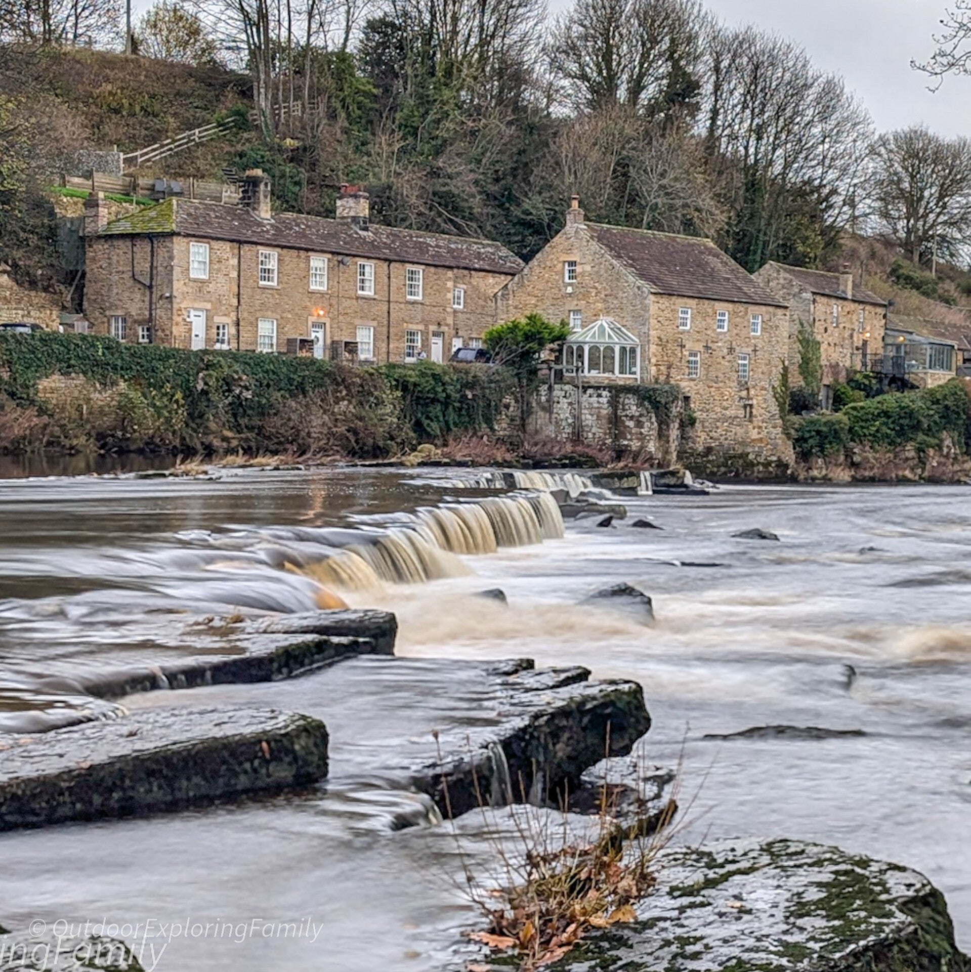 The old weir on the River Tees in Barnard Castle with water flowing over the stones on the riverside walk.