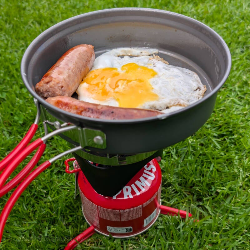 Lightweight camping stove cooking sausage and egg during an outdoor walk