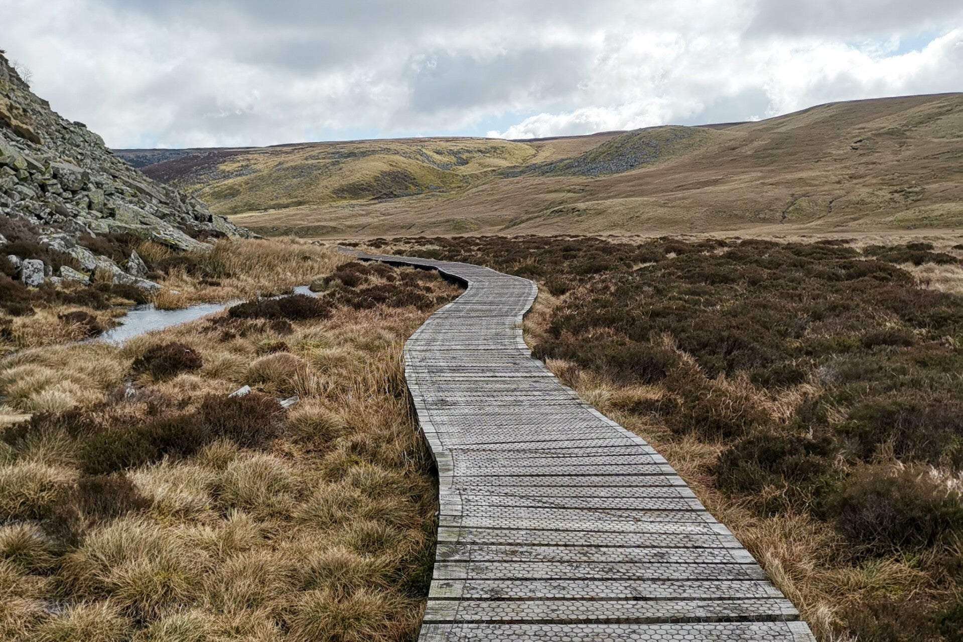 Wooden boardwalk crossing open moorland on the Cow Green circular walk in Upper Teesdale with wide valley views under cloudy skies