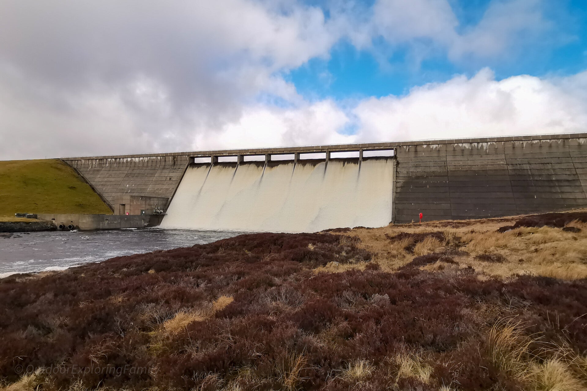 Cow Green Reservoir dam overflow in Upper Teesdale with water pouring over the concrete structure across open moorland