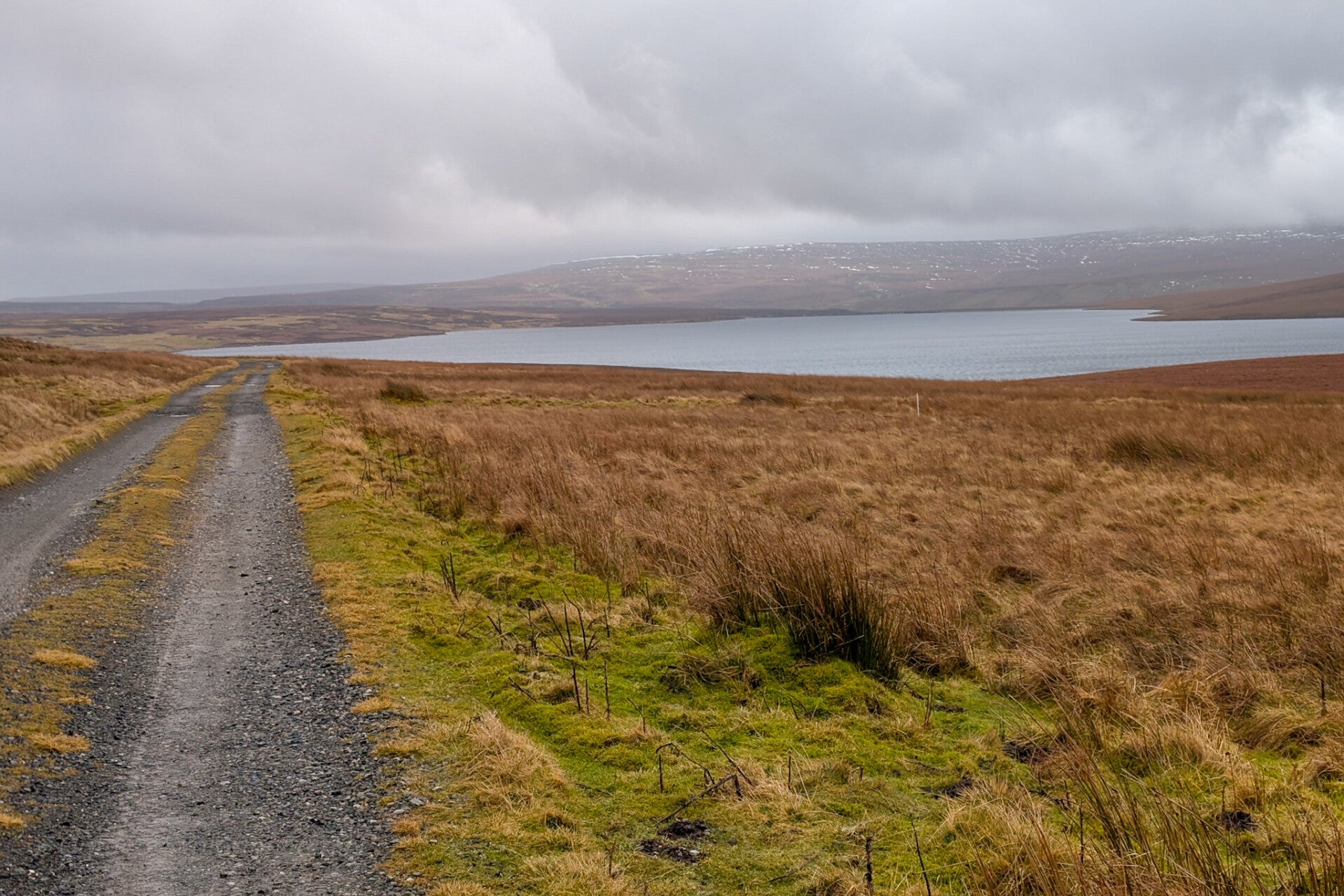 Gravel track on the Cow Green history walk leading beside Cow Green Reservoir in Upper Teesdale with moorland and distant hills