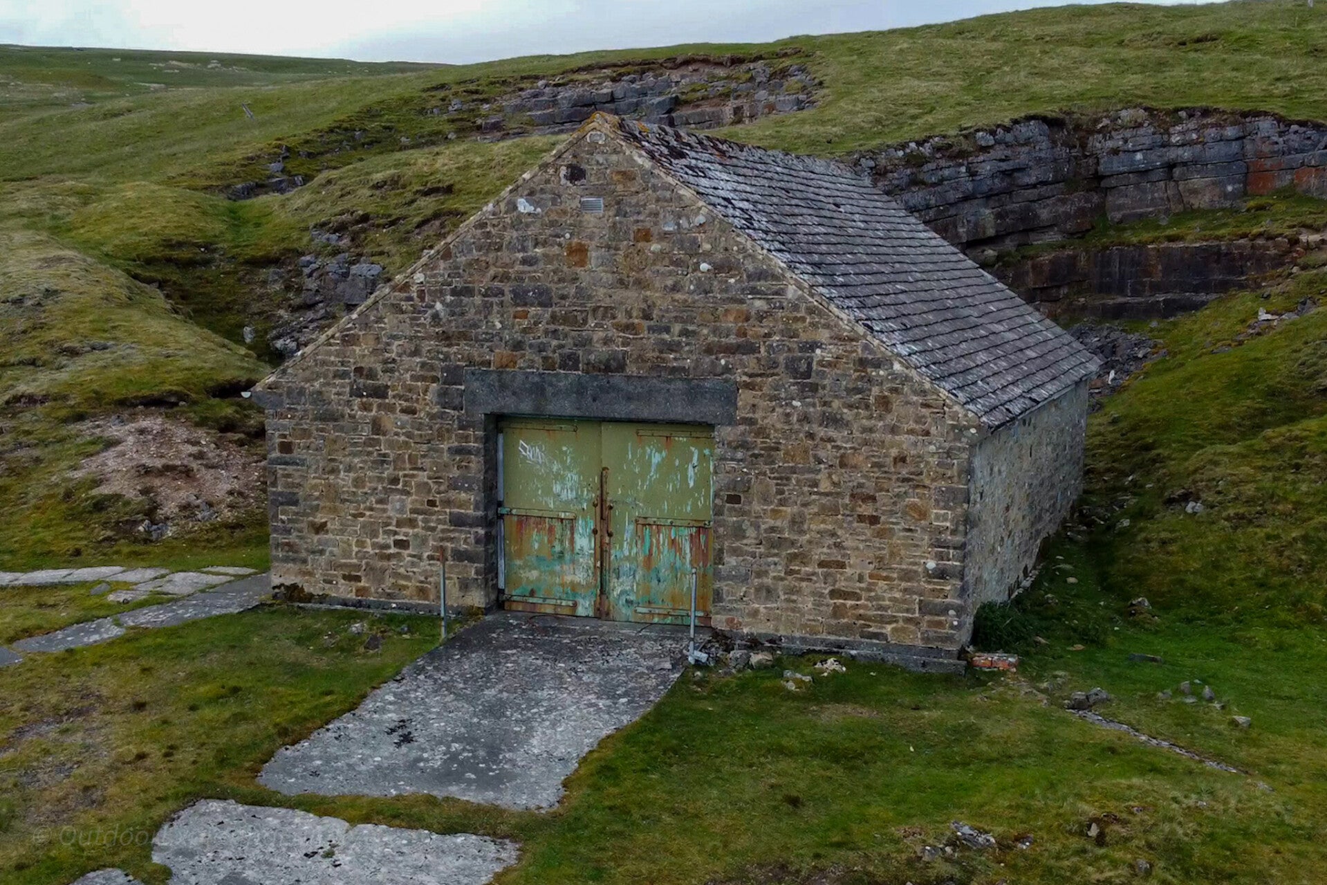 Old boathouse at Cow Green Reservoir in Upper Teesdale, a stone building set into the hillside beside rocky ground