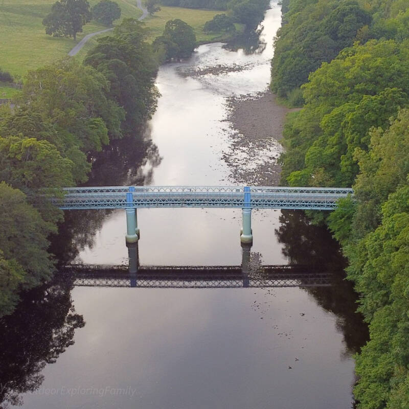 Deepdale Aqueduct reflected in the River Tees, showing the cast iron bridge structure and support columns near Barnard Castle.