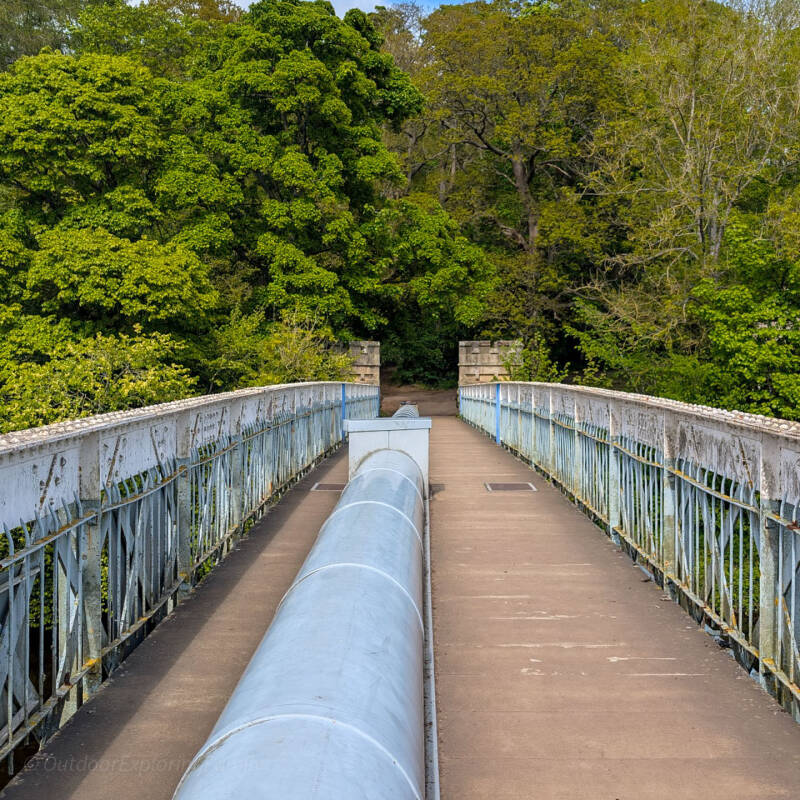 View along Deepdale Aqueduct towards Deepdale woods, showing the footbridge, water pipe and iron railings.