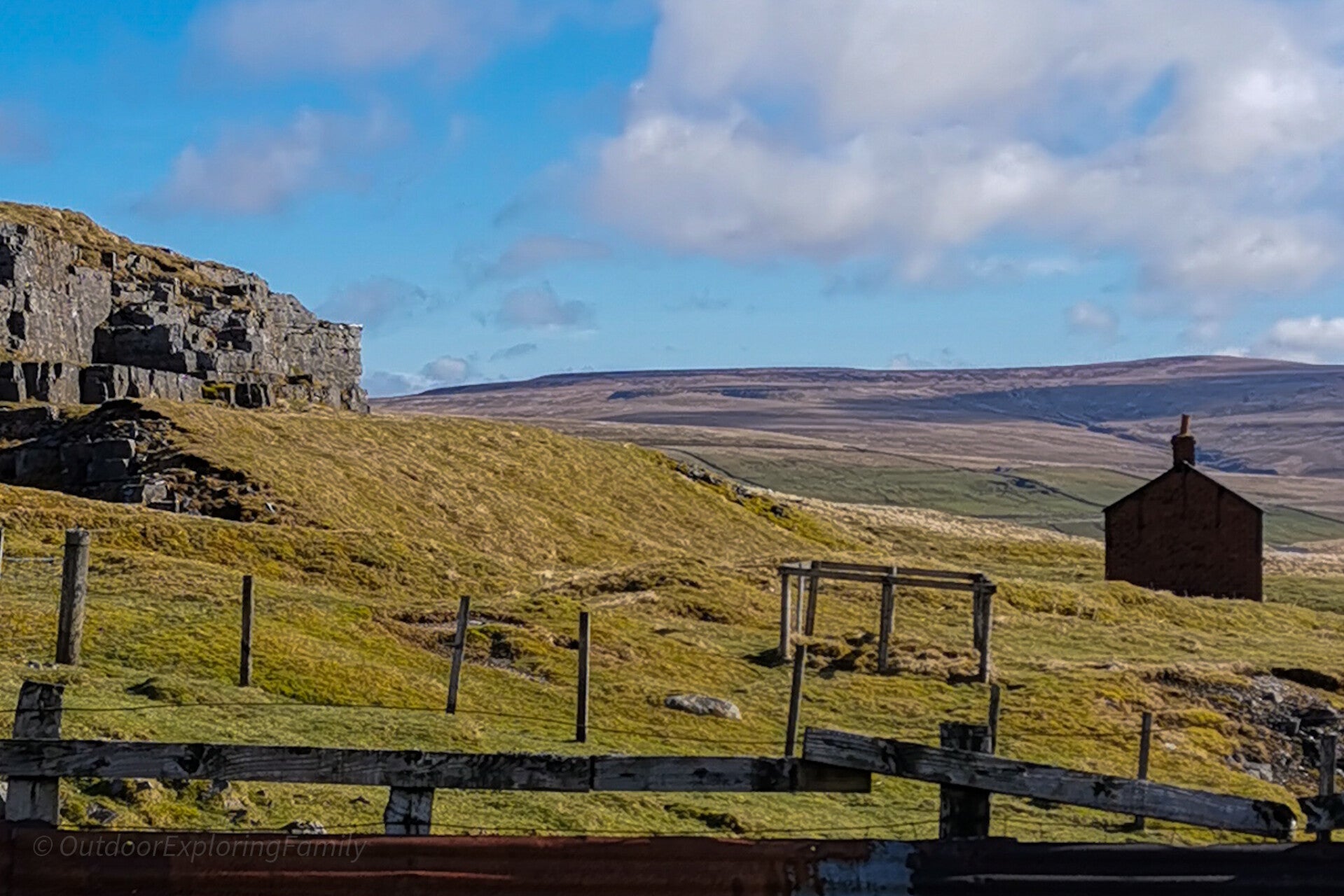 Views across East Cow Green Mine in Upper Teesdale with rocky outcrops, open moorland and a small red building in the distance