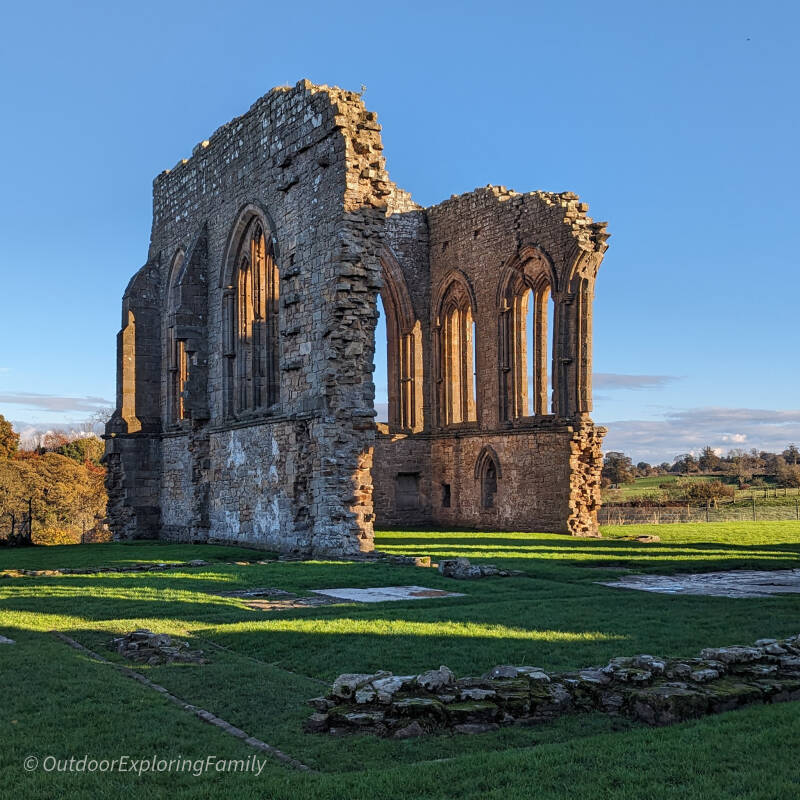 Tall stone church walls and arched window openings at Egglestone Abbey with green grass in the foreground