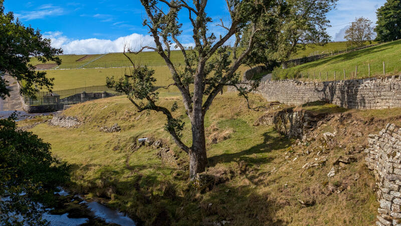 Old stone walls and grassy ground around the recorded Hury Mill site below Hury Reservoir dam in Baldersdale.