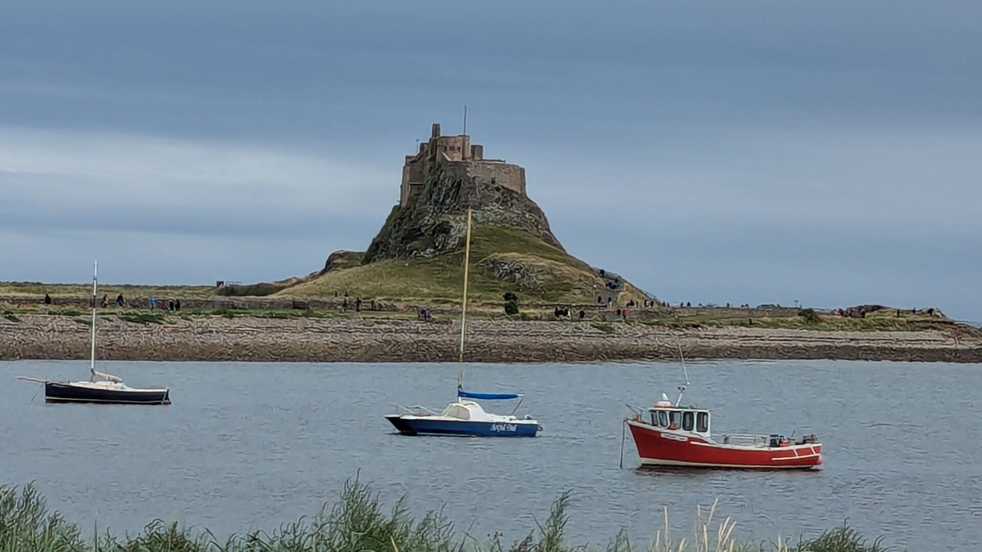 Lindisfarne Castle on Holy Island seen across the harbour with boats on the water, Northumberland